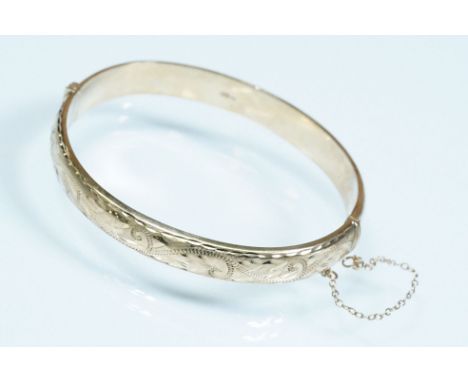 9ct gold hinged bangle bracelet having a foliate engraved front with tongue in groove clasp. Hallmarked Birmingham 1989. Meas