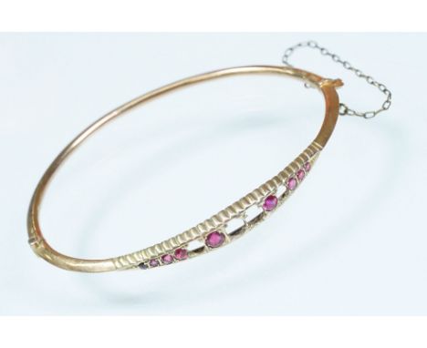 9ct gold and pink paste bangle bracelet being set with round cut pink paste stones (some missing) with a hinged opening. Mark