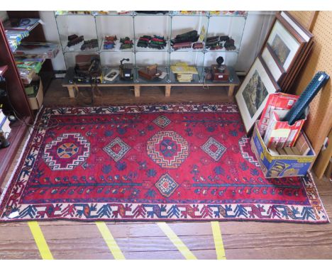 A Persian village rug, with allover medallion and tree design on an red ground with geometric ivory border, 215 x 130 cm 