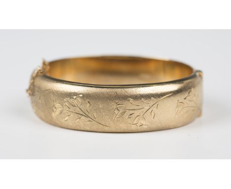 A 9ct gold oval hinged bangle, the front engraved with floral sprays against a textured ground, on a snap clasp, fitted with 