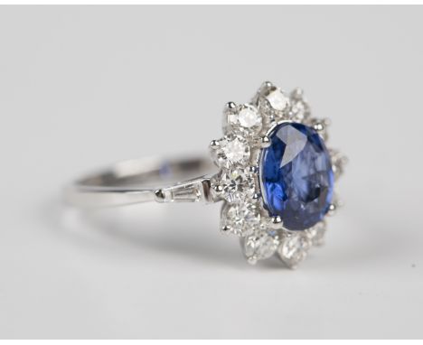 An 18ct white gold, sapphire and diamond oval cluster ring, claw set with an oval cut sapphire within a surround of circular 