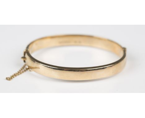 A 9ct gold oval hinged bangle on a snap clasp, fitted with a safety chain, Birmingham 1973, weight 11.4g, inside width 6cm.Bu