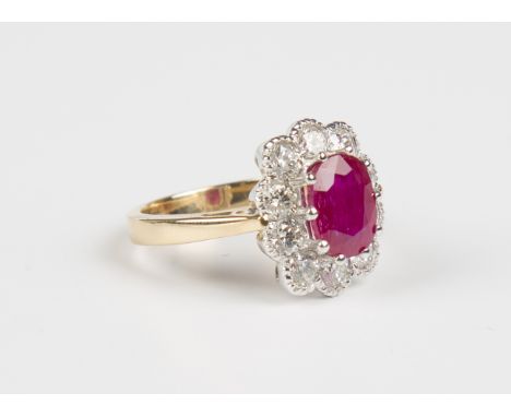 An 18ct gold, ruby and diamond oval cluster ring, claw set with an oval cut ruby within a surround of ten circular cut diamon