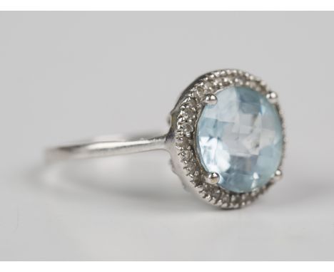 A 9ct white gold, blue topaz and diamond ring, claw set with the circular cut blue topaz within a surround of circular cut di