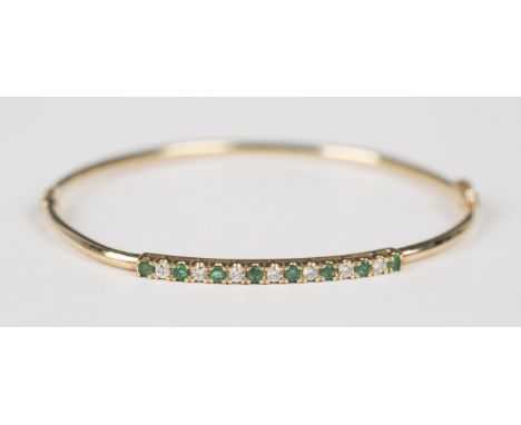 A 9ct gold, emerald and diamond oval hinged bangle, mounted with alternating circular cut emeralds and diamonds, import mark 