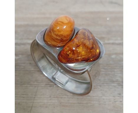 A white metal bangle set with two large chunks of amber and butterscotch amber.