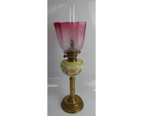 A Victorian brass oil table lamp, with painted reservoir and graduated cranberry tinted shade, the duplex burner now with ele