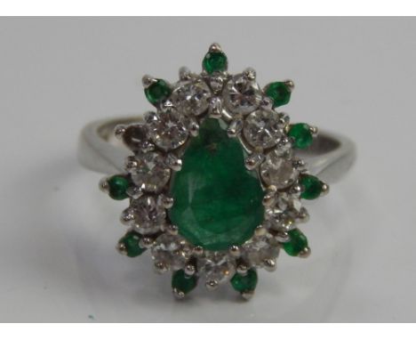 An 18ct white gold dress ring, with emerald and diamond set cluster, with central pear shaped emerald surrounded by tiny diam