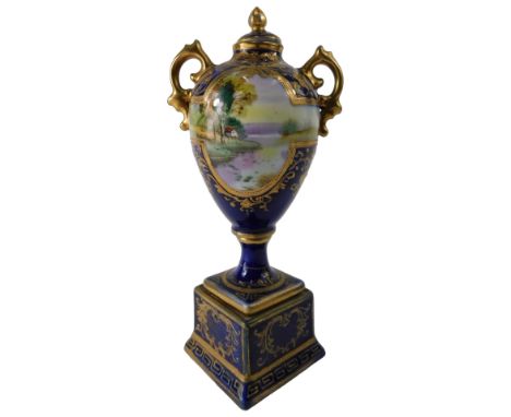A Noritake two handled urn and cover, decorated with river landscape, on a cobalt blue ground, with integral square plinth, 1