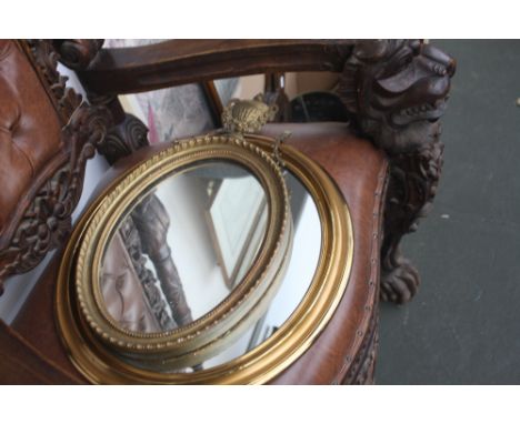 An oval gilt framed mirror with urn and swag finial and bead border, with an oval mirror