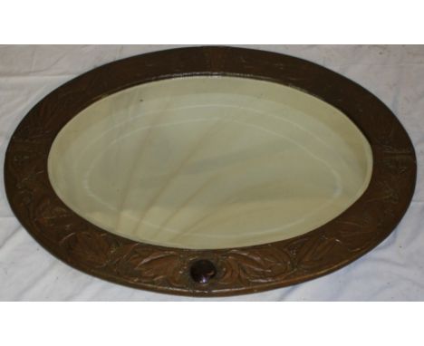 An unusual bevelled oval wall mirror in embossed copper relief decorated frame, decorated with birds, leaves and berries and 
