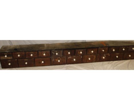 A old bank of twenty-one stained pine drawers with ceramic handles, 109" long x 13½" high 