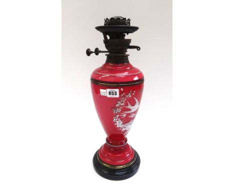 A Victorian cranberry glass oil lamp with white enamel decoration depicting swallows in flight within a foliate shaped border