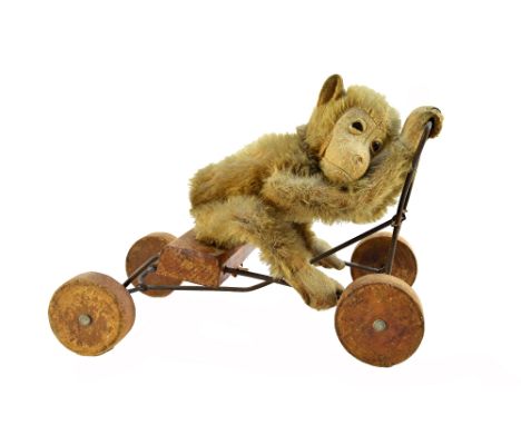 A Steiff peddling monkey, pre-war, with golden fur and jointed limbs, on a wire work wooden mounted frame, 28cm wide.  Illust