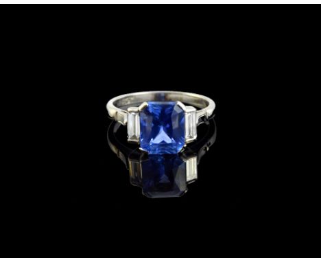 A platinum, sapphire and diamond set three stone ring, claw set with the cut cornered rectangular cut Ceylon sapphire at the 