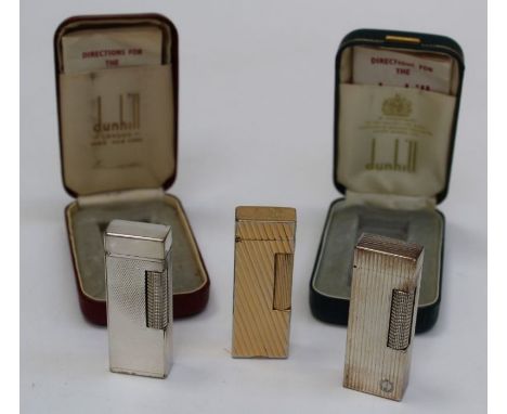 A trio of textured Dunhill vintage lighters, two in silver tone in cases with instructions plus a gold tone lighter in pouch 