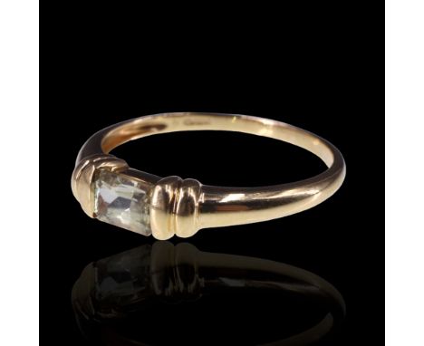 A pale yellow topaz finger ring, the emerald cut stone clinched between paired collars on an 18 ct gold shank, R/S, 2.4 g