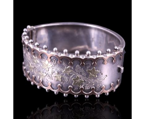 A Victorian silver hinged cuff bangle faced with two colours of gold engraved in depiction of a vine of ivy within cusped and