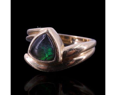 An ammolite ring, comprising a trilliant cabochon bezel-set between the cross-over double reeded shoulders of 14 ct gold shan