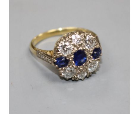 A Victorian style 18ct, three stone sapphire and six stone diamond set circular cluster ring, with diamond set shoulders, siz