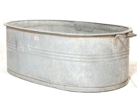 A vintage 20th century industrial yard reclaimed galvanised oval twin handled bath having reinforced rings around and drainin