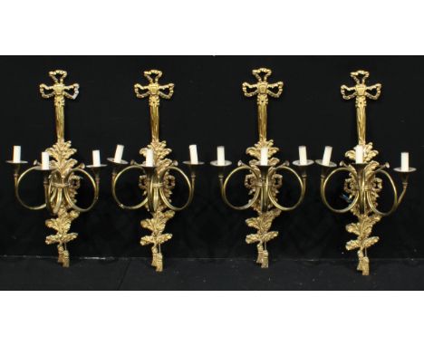 A set of four gilt metal three light side lights, each with scroll trumpet arms, ribbon tied acanthus leaf backs, 80cm long, 