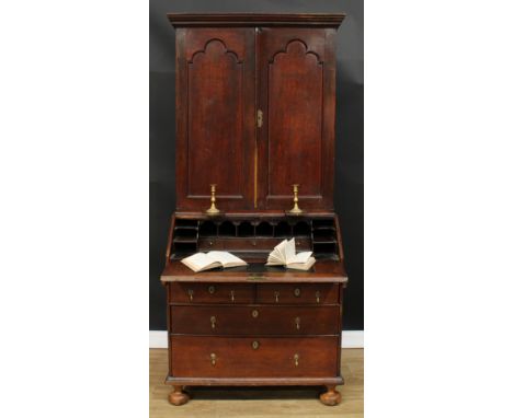 An early 18th century oak bureau book cabinet, moulded cornice above a pair of trefoil-arch panel doors enclosing pigeonholed