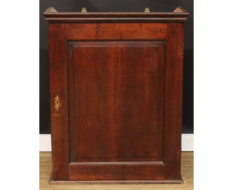 A George III oak wall hanging livery or provision cupboard, moulded cornice above a raised and fielded panel door enclosing t