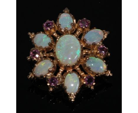 A 9ct gold ruby and opal starburst pendant/brooch, the central polished oval opal cabochon surrounded by six further smaller 