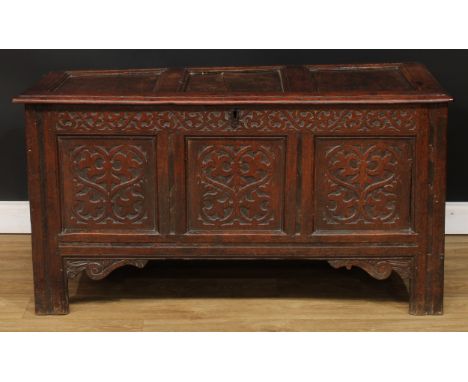 An early 18th century oak blanket chest, hinged three panel top, the frieze and front panels incise carved with scrolling lea