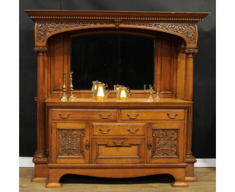 An Arts &amp; Crafts oak sideboard, outswept cornice with dentil capital above an apron carved with leafy C-scrolls, the supe