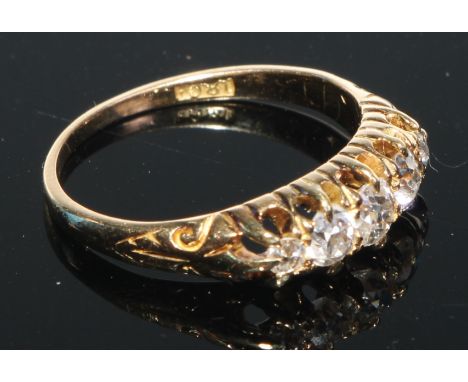 An 18ct gold graduated five stone diamond ring, brilliant cut claw set stones, open bezel with engraved scroll shoulders, rin