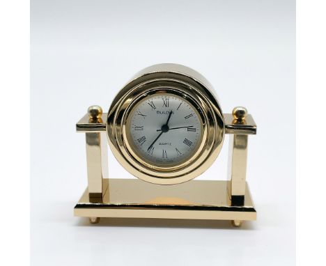 This elegant Bulova mini table clock features a classic design with a gold-tone finish. The round clock face is adorned with 