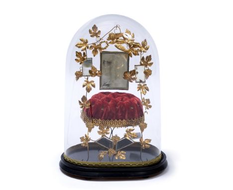 A FRENCH 'DOME DE MARIAGE' with gilt vine leaves around a mirror and a velvet cushion, all beneath a glass dome with ebonised