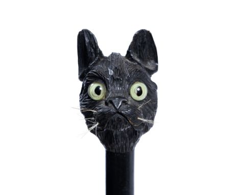 AN EBONISED WALKING STICK with a carved wooden top in the form of a cat's head with glass eyes, in the style of Louis Wain