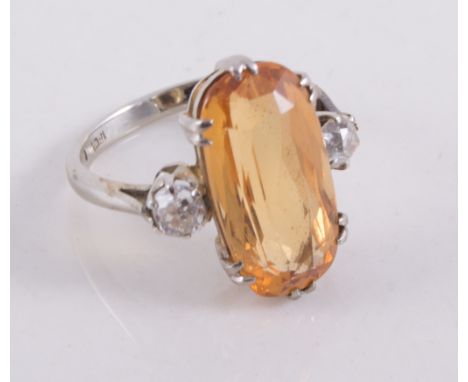 A lady's three stone dress ring, the oval golden faceted stone 17cm x 10cm, double claw set with an old brilliant cut diamond