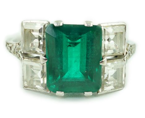 An Art Deco platinum, emerald and square cut diamond dress ring, with diamond chip set shoulders, the emerald measuring appro