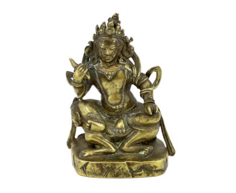 * A Tibetan gilt bronze figure of a deity, 17th century, holding a purba in his right hand, seated on a corpse, rockwork base