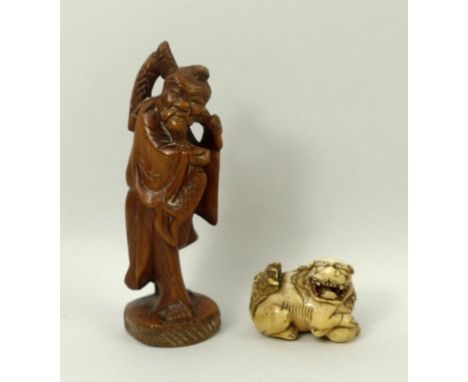 A Japanese netsuke in the form of a Shishi lion with raised paw and ball, 3 by 2 by 2.5cm, and a wooden carved figure of a fi