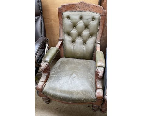 An Edwardian library chair with a green leather button upholstered back, with a pad seat and arms, carved with lions heads on