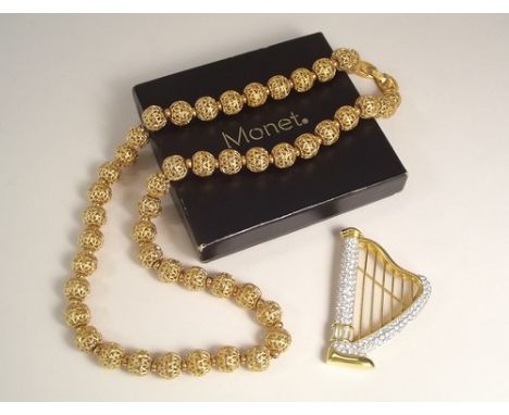 SWAROVSKI & MONET.
A Swarovski crystal set harp brooch, 6cm & a Monet gold tone filigree bead necklace, boxed.
