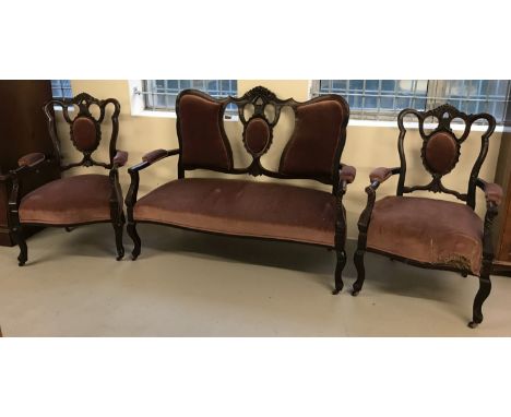 A Victorian 2 seater wooden framed settee with 2 matching arm chairs. With carved detail to seat backs, dark pink velvet upho