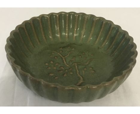 A small green glazed ceramic shallow bowl with scalloped edge and blossom detail.  Approx. 4cm tall x 13cm diameter.