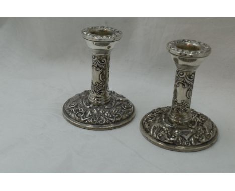 A pair of silver candle sticks of short form having bird and mask repousse decoration with plain cartouche and weighted bases