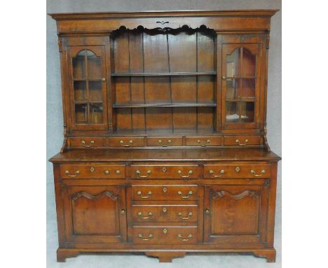 A Georgian style oak dresser the upper glazed and shelved section above base fitted with cupboards and drawers on bracket fee