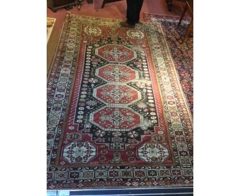 A CAUCASIAN RED GROUND SMALL CARPET with a central interlocking quadruple medallion within a black ground field of flower hea