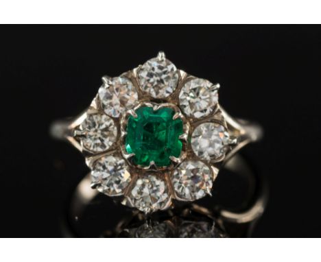 An emerald and diamond mounted circular cluster ring: with central 'emerald-cut' emerald approximately 5.5mm x 5.0mm claw-set