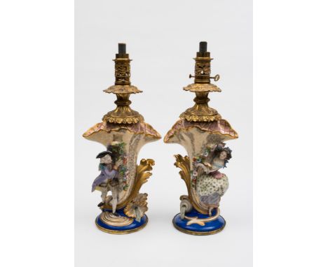 A pair of French porcelain lamps: each modelled with a bisque male and female figure grasping a floral garland and standing b