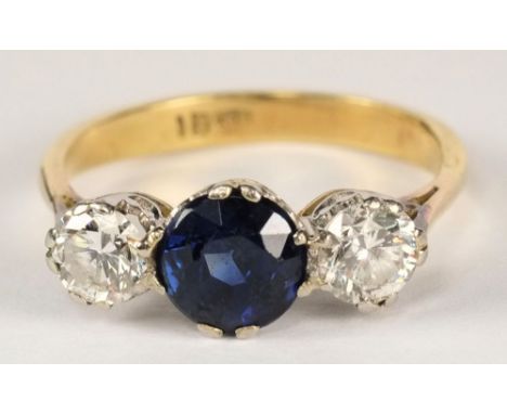 An 18ct gold, sapphire and diamond three stone ring:, the circular sapphire between brilliant-cut diamonds estimated to weigh