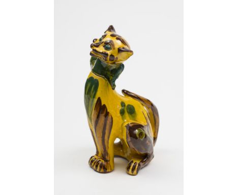 A C.H. Brannnam (Barnstaple) pottery cat: modelled seated with grinning visage and sporting a bow tie with chocolate and gree